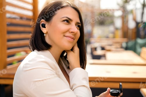 Preview: Woman inserts an earpiece into her ear to listen to music from her smartphone.