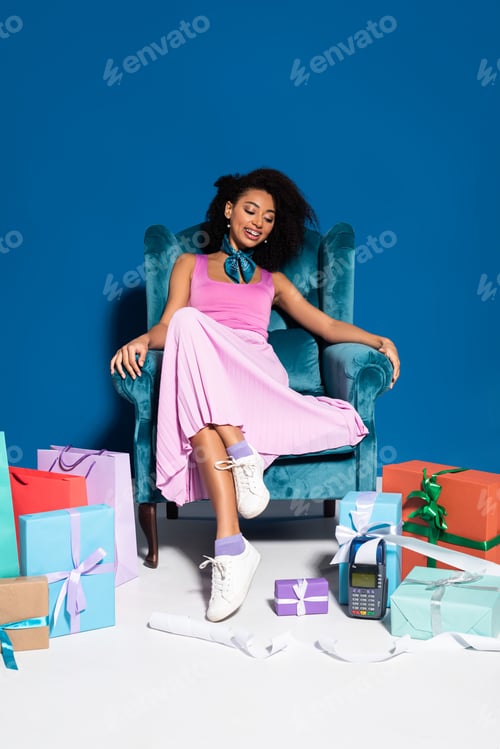 Preview: smiling beautiful african american woman sitting in velour armchair near payment terminal with