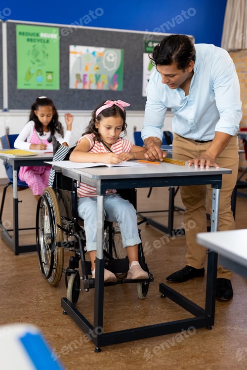 Preview: Happy biracial male teacher with girl in wheelchair in class at elementary school