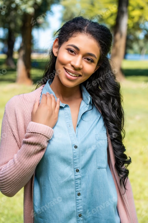 Preview: smiling attractive african american woman posing in park and looking at camera