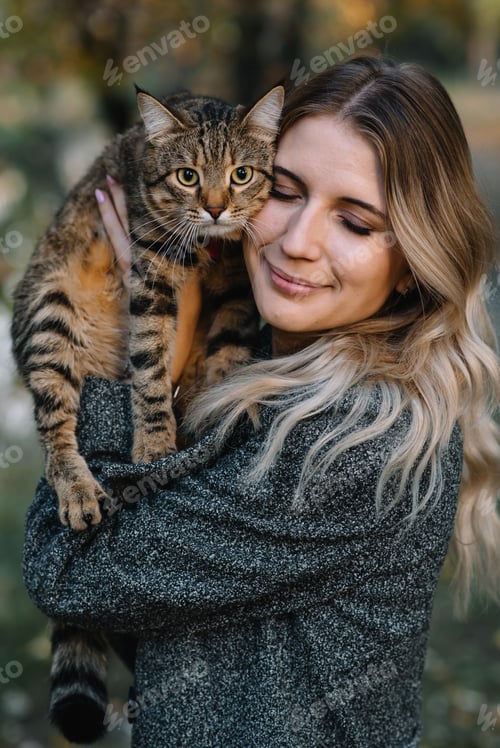 Preview: girl and a cat in the autumn park.a woman in a brown sweater walking with her gray cat