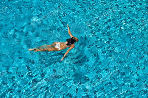 Preview: Top view of young woman swimming in infinity swimming pool