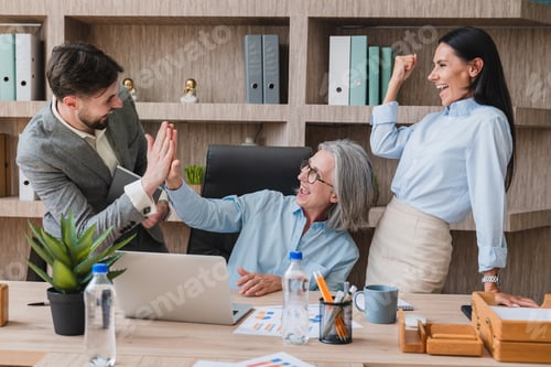 Preview: Smiling Business Team Celebrating Accomplishment With Joyful High-Five Gesture in Office