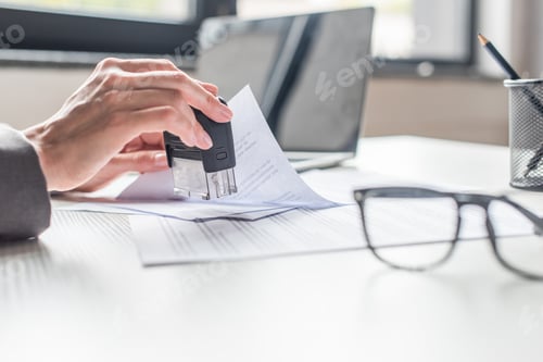 Preview: Cropped view of businesswoman putting stamp in document at workplace on blurred background