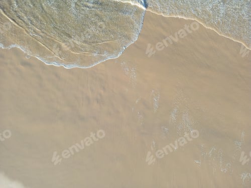Vorschau: Luftaufnahme von sanften Wellen, die den Sandstrand überfluten