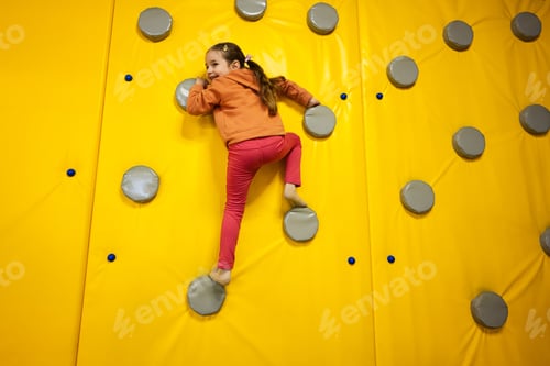 Preview: Little girl kid climbing wall at yellow playground park.
