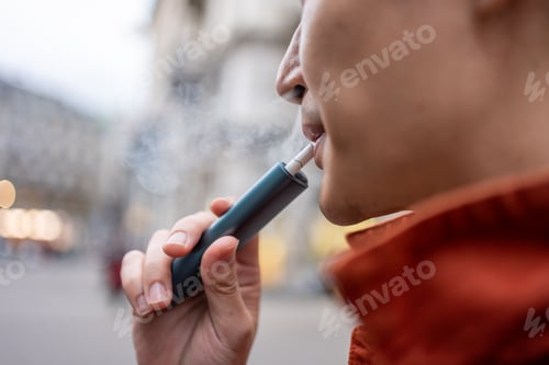 Preview: Close up of a man vaping with electronic cigarette outdoor on street.