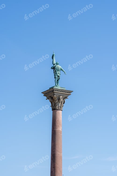 Vista previa: Statue of a Roman soldier atop a column against a clear blue sky