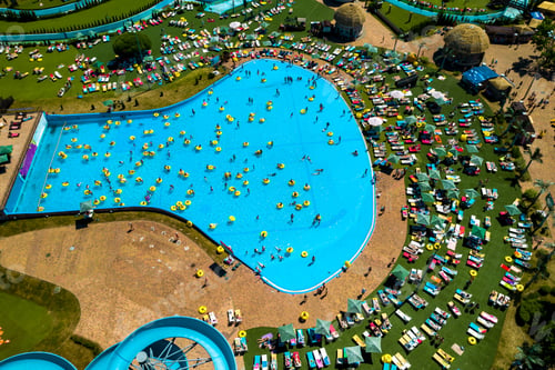 Preview: Top view of people relaxing in the pool on yellow inflatable circles and sun beds on the beach