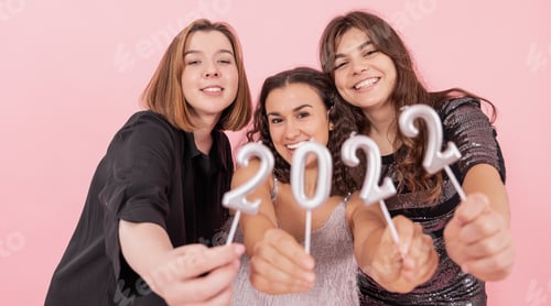 Visualização: Um grupo de garotas está segurando velas dos números 2022 em um fundo rosa.