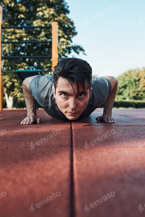Preview: Young man doing push-ups on a red rubber ground during his workout in a modern calisthenics park