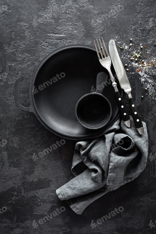 Preview: Empty cast-iron pan with cutlery on dark background for restaurant menu, top view
