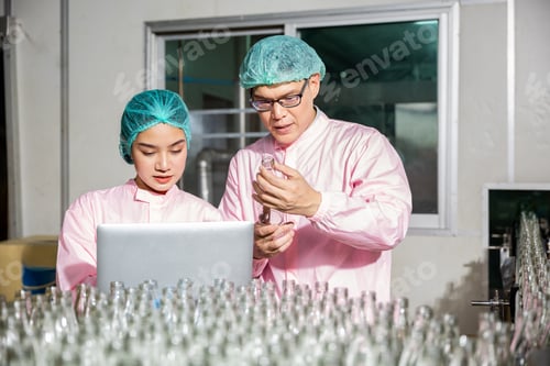 Preview: Two engineers oversee quality control checking product bottles on a beverage factory's conveyor belt