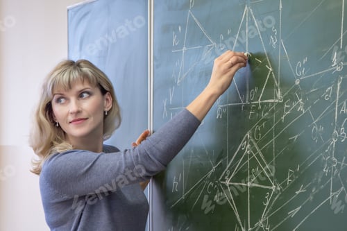 Preview: Young woman teacher writes on the blackboard with chalk closeup