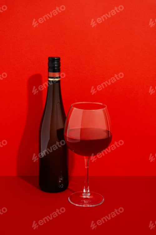 Preview: Bottle and glass of wine. Alcoholic drink on red background with deep shadows
