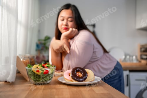 Preview: Asian young plus-size woman deciding between green salad and donut.