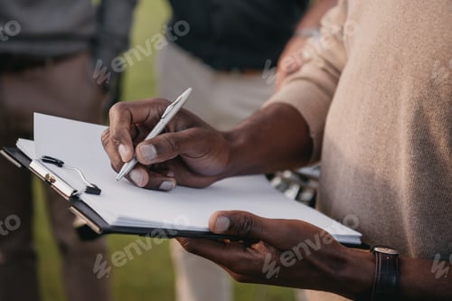 Preview: cropped view of african american man writing something on paper in clipboard