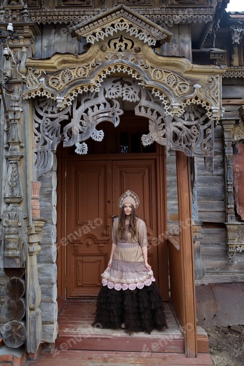 Preview: Russian Tourist Girl In Kokoshnik And Richly Decorated Carved Porch Door Of Traditional National