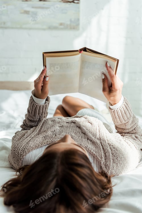 Preview: selective focus of woman in grey sweater reading book at morning
