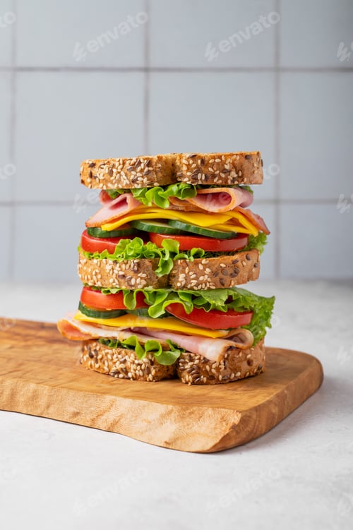 Preview: A triple sandwich with ham, cheese, lettuce, and vegetables on whole grain bread on a wooden board