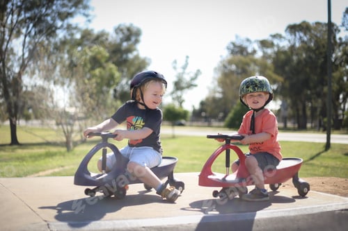 Preview: Cute and adorable blonde Australian kids with helmets riding a children's car in the playground