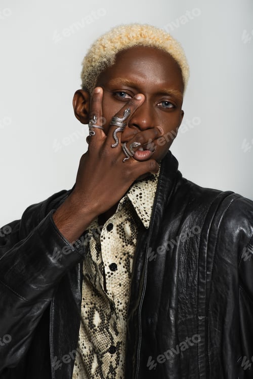 Preview: stylish african american man in snake-shaped rings posing with hand on face isolated on grey