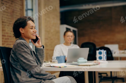 Preview: Female manager is talking phone with client while sitting in coworking on colleague background