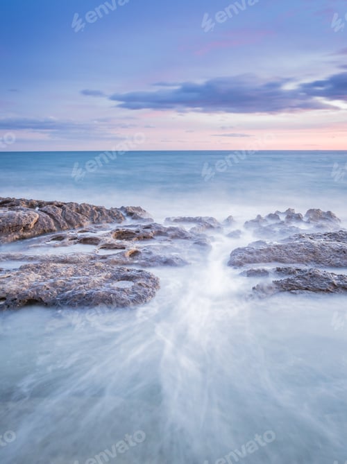Aperçu: Sea waving near rough rocks during sunset