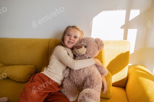 Preview: Little girl happily hugging plush teddy bear on sofa