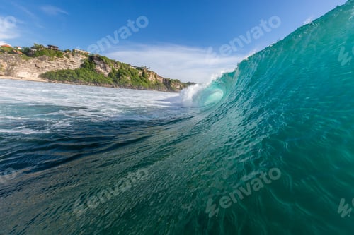 Preview: Closeup of a sea wave surrounded by mountains and greenery under a blue sky in Uluwatu in Bali