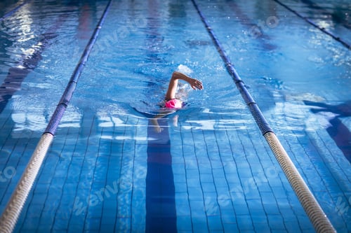 Preview: Senior female swimmer gliding through tiled pool lane by lane ropes in pink swim cap goggles