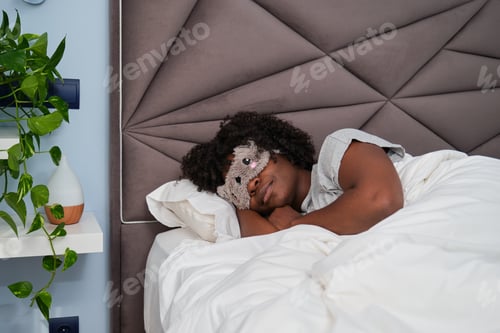 Preview: African young woman sleeping with a cute sleep mask in a room with a plant.