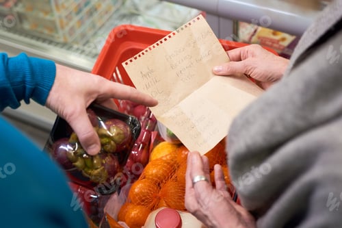 Preview: Overview of hand of mature man pointing at shopping list held by his wife