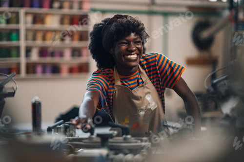Preview: Happy interracial graphic technician operating silk screen printing press