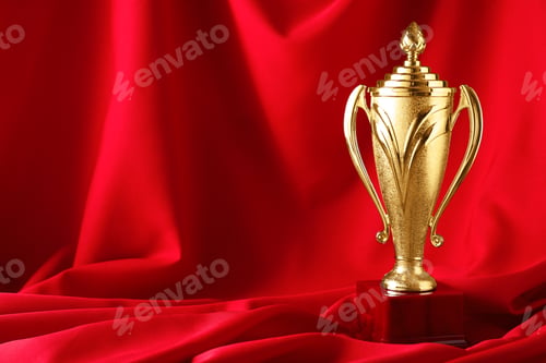Preview: Golden trophy cup on red fabric. Space for text