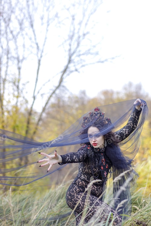 Preview: A woman dressed as a witch stands in an autumn forest. A Gothic queen on Halloween.