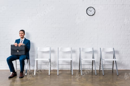 Preview: Smiling man with briefcase waiting for interview while sitting on chair