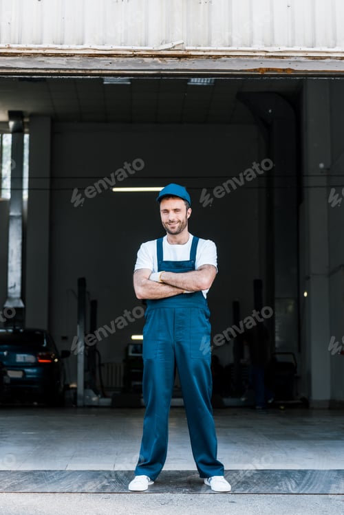 beau mécanicien automobile barbu debout avec les bras croisés