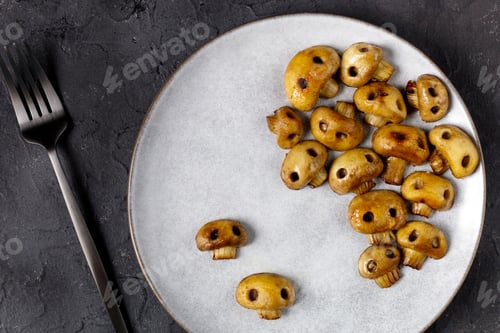 Preview: Round plate with mushrooms in the form of skulls and fork on white table. Edible Halloween Concept