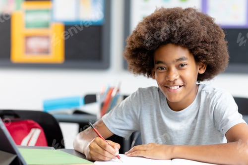 Preview: Portrait of smiling african american schoolboy with afro, at desk writing in class, with copy space
