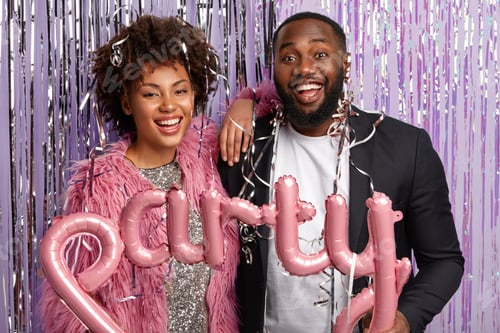 Preview: Horizontal shot of optimistic couple pose together with tinsel and balloons, express good emotions,