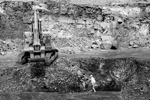 Preview: Black and white shot of a worker and an excavator in a rocky quarry.