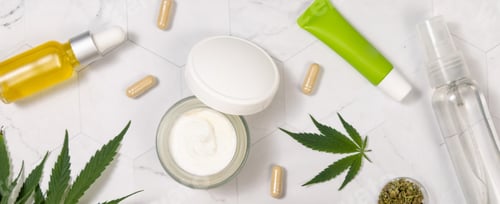Preview: Cosmetic bottles, jars and tubes with blank label near green cannabis leaves. Mockup