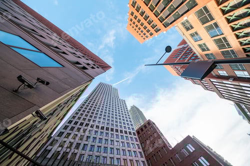 Preview: Looking up at a blue sky between a canyon of modern highrise buildings.