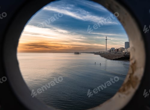 Preview: Scenic view of the ocean and a coastal town at sunset from a porthole.
