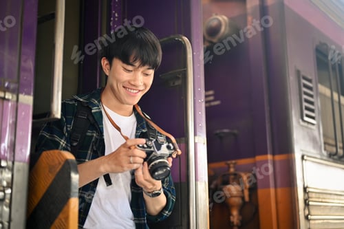Preview: Happy male tourist with backpack checking photo on camera at the railway station