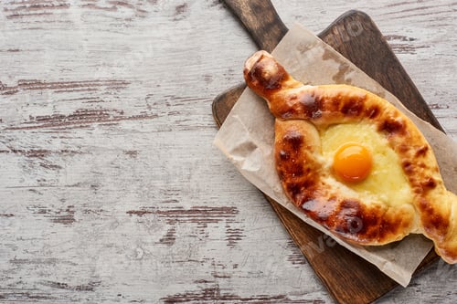 Preview: Top view of traditional adjarian khachapuri on cutting board on wooden texture