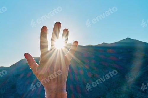 Preview: Anonimus hand holding sunlight, bright sun's rays pass through the fingers over mountain background
