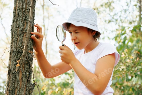 Preview: Cute adorable Caucasian girl kid looking at tree in forest through magnifying glass.