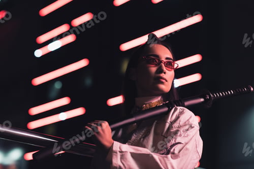Preview: low angle view of attractive asian girl in white kimono holding japanese sword on street with neon